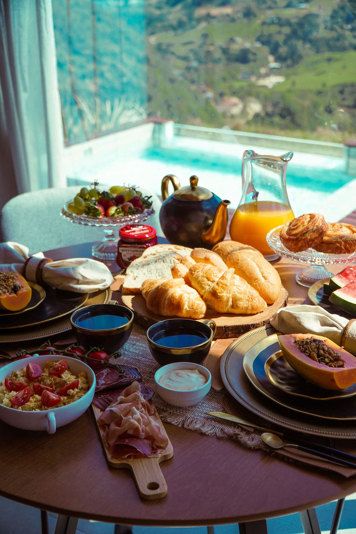 Mesa posta com pães, frutas e café diante da janela com vista para o vale